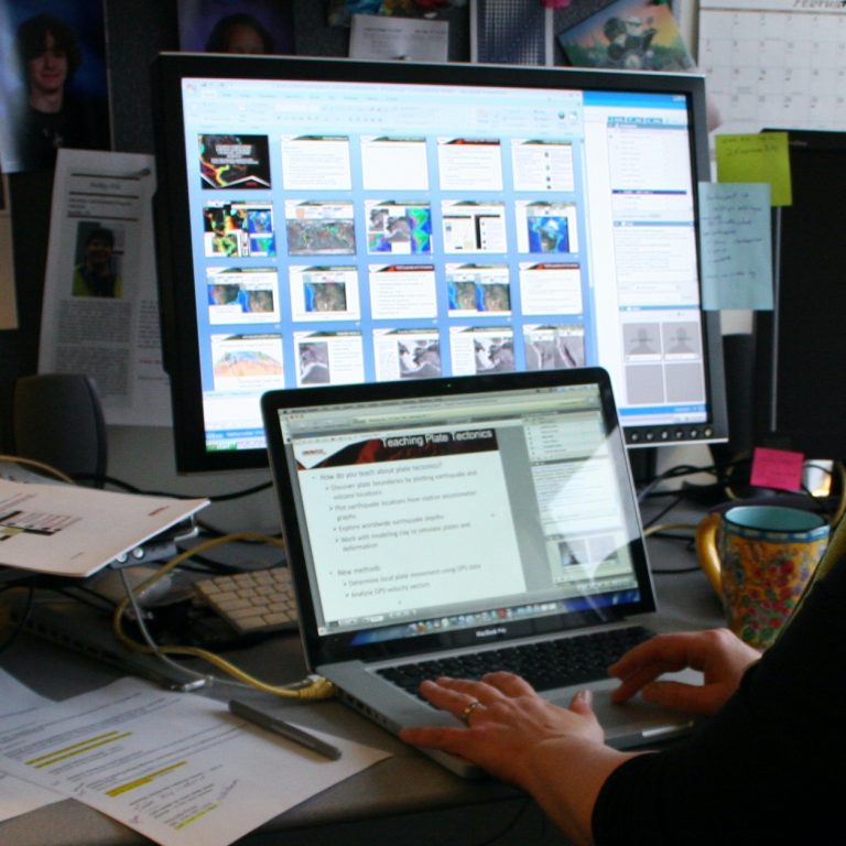 someone is typing on the keyboard of a laptop with a monitor in the background