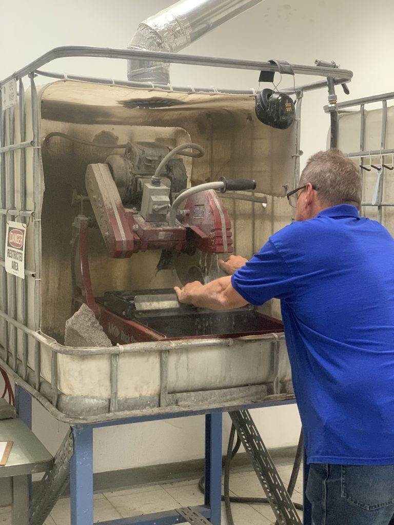 NSF Ice Core Facility employee cutting a granite sample with a drill at the NSF Ice Core Facility.