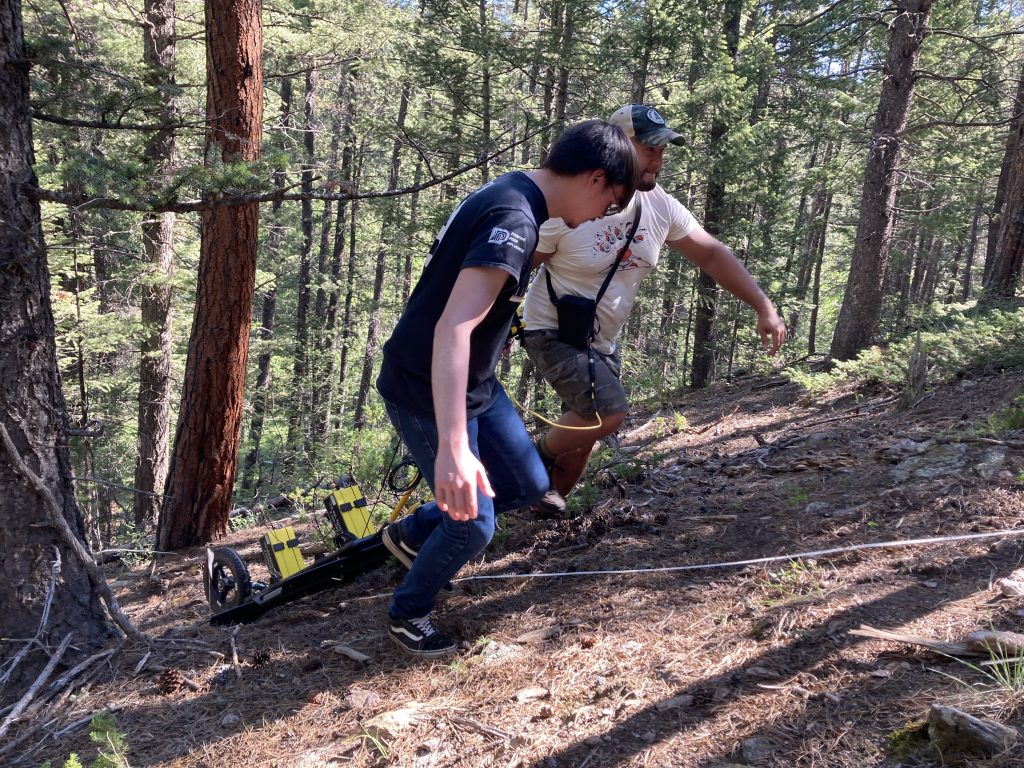 Alex Nguyen and another lab member pulling a GPR instrument up a hill in a forest