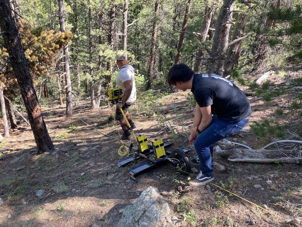 Alex pulling the GPR instrument uphill while another lab member pushes it at the same time.