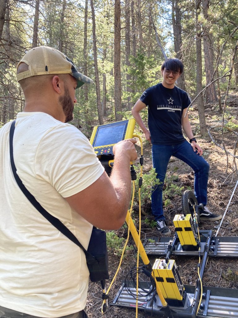 Alex Nguyen takes a break from pulling the GPR instrument while another lab member looks at the screen of the GPR instrument.