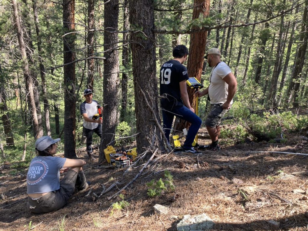 Four people work to pull a GPR instrument with a yellow robe up a hill in a forest