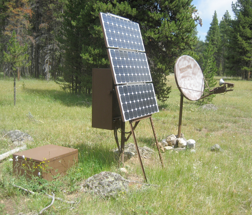 solar panel from side with enclosure attached to back of panel and another enclosure nearby in the ground