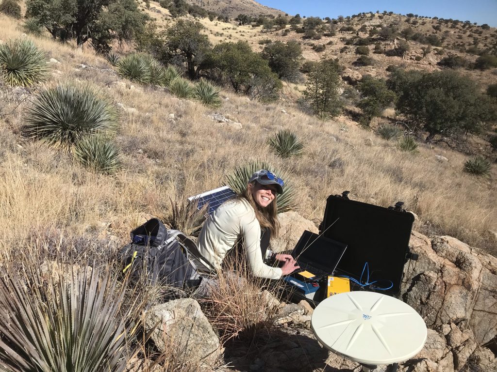 Cassie Hanagan crouching down to work with equipment in the field for her PhD.