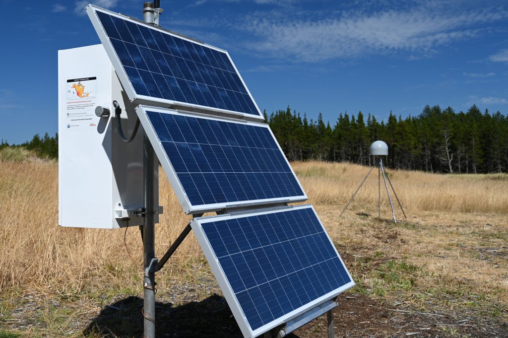 solar panels on enclosure box with antenna behind and trees in the background