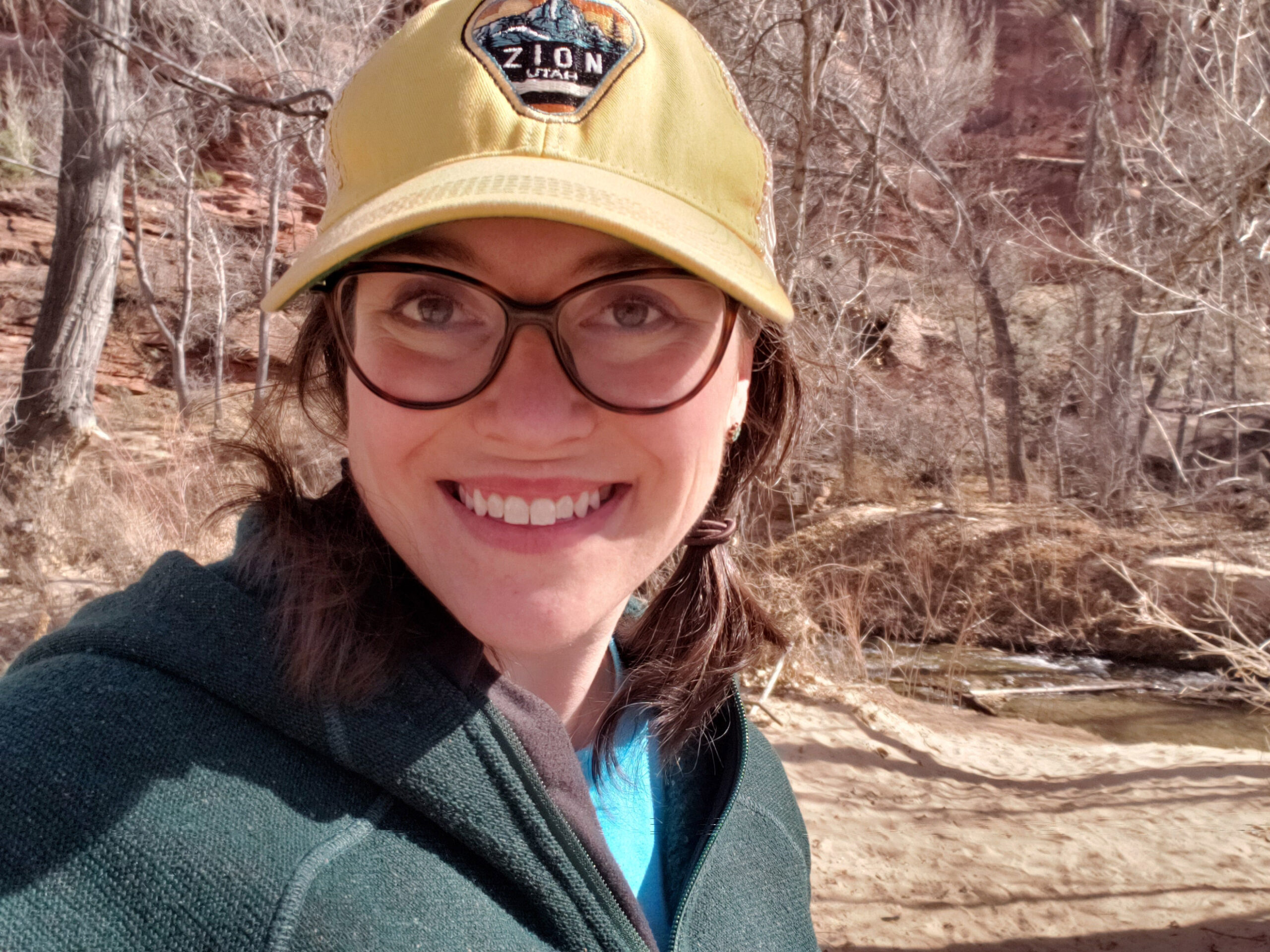 photo of woman wearing glasses and hat, trees in backgrund