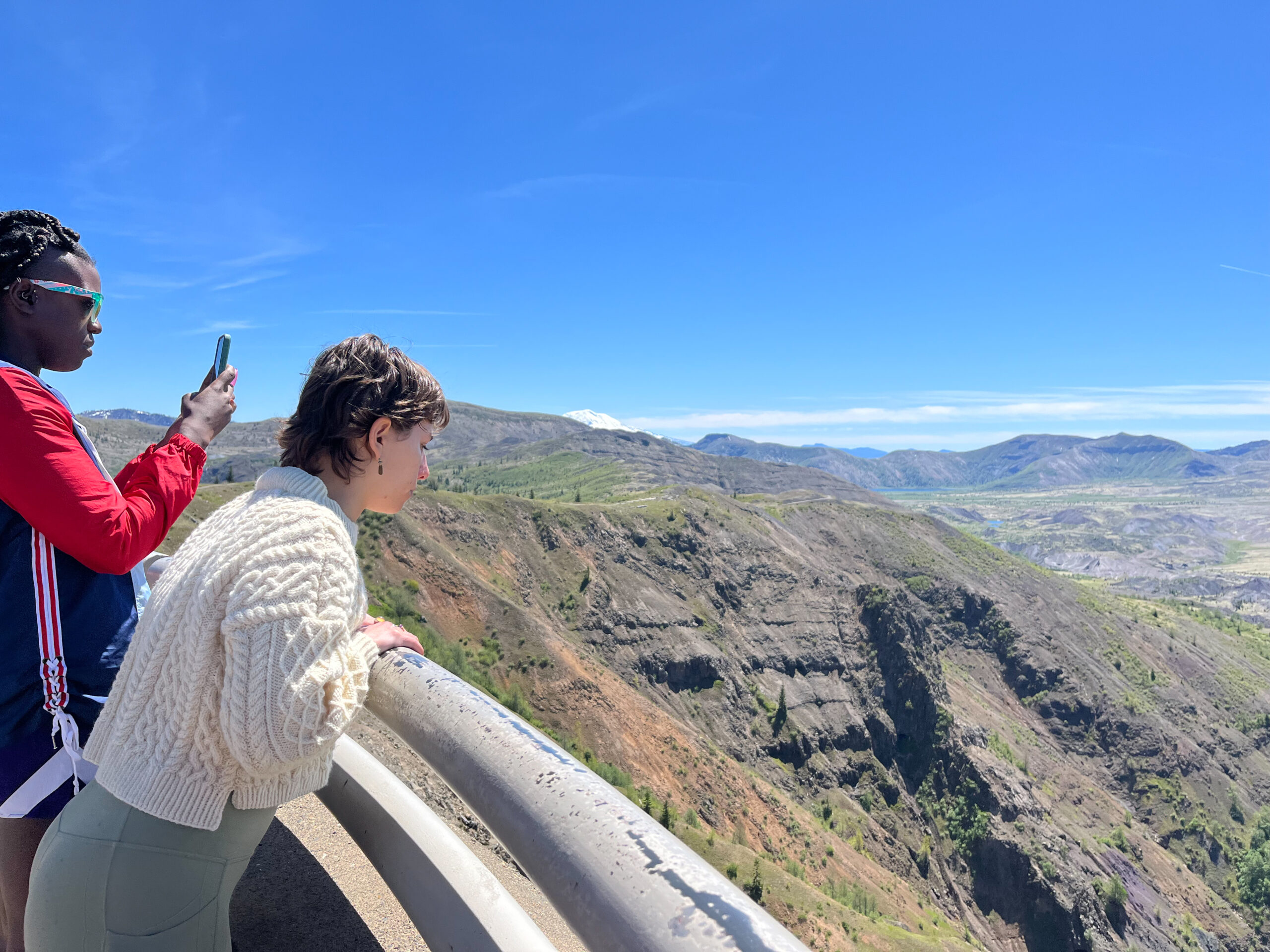 Anika Knight snaps a photo while 2022 RESESS Satellite Intern Angie Bonanno looks over the railing at Mount St. Helens on the RESESS Satellite group from the University of Washington field trip to Mt St Helens (Photo: Lucia Bellino/UNAVCO)