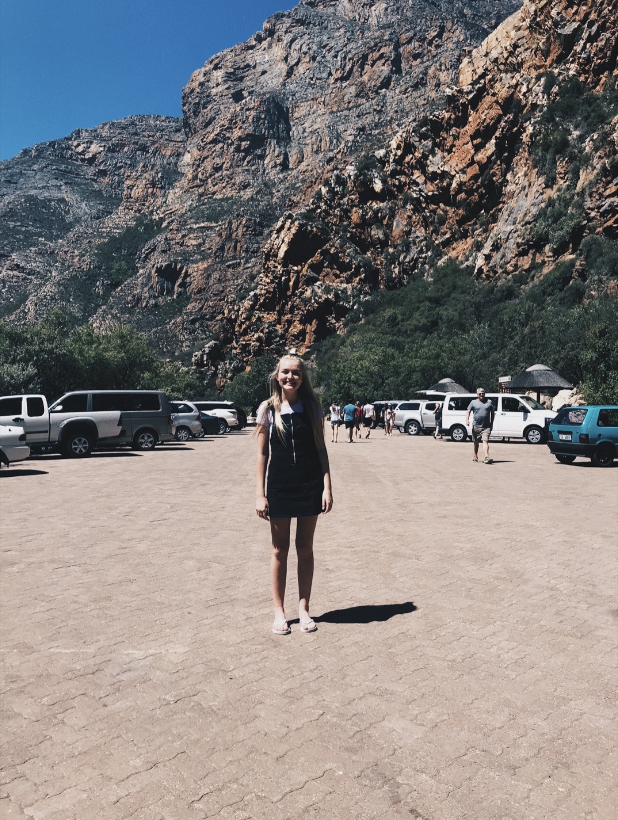 RESESS intern Courteney Pike stands in the parking lot of Meiringspoort Pass in the Western Cape province in South Africa with huge rock outcrops visible in the background.