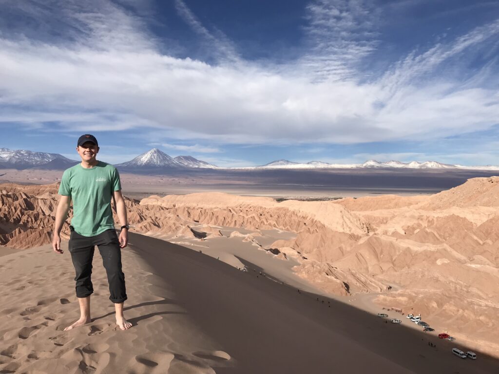 USIP Intern Cole Speed stands atop an aeolian sand dune near Valle de la Luna in the Atacama Desert, northern Chile. Mountains are visible in the background.