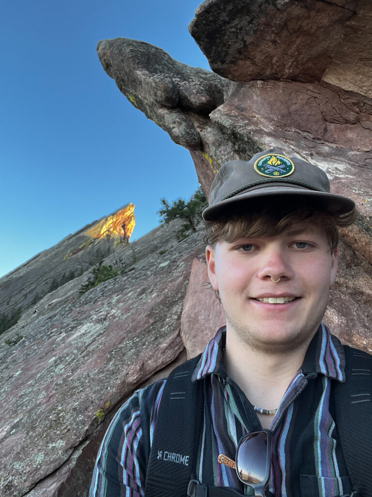 Selfie of USIP Intern Ian Sulley in front of very slanted outcrops of rock.