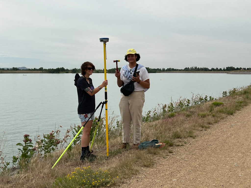 Geo-LaunchPad Interns Taryn Roby (left) and Kyle Albrecht (right) stand with a portal GPS antenna. Taryn is holding the monument and Ky is holding a mallet.