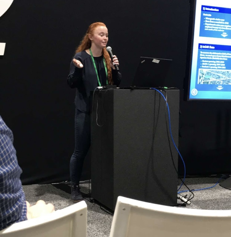 USIP Intern Becca Bussard speaking during her presentation with a microphone in hand at the 2021 Annual AGU conference in New Orleans, LA.